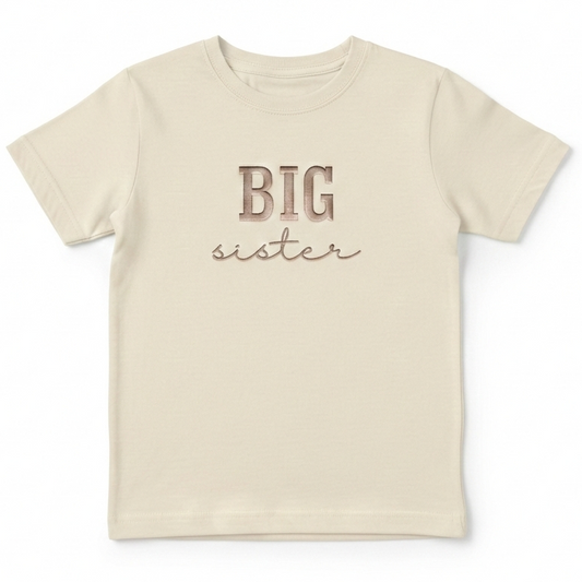 A beige T-Shirt with the words "Big sister" embroidered on the front in rose gold thread