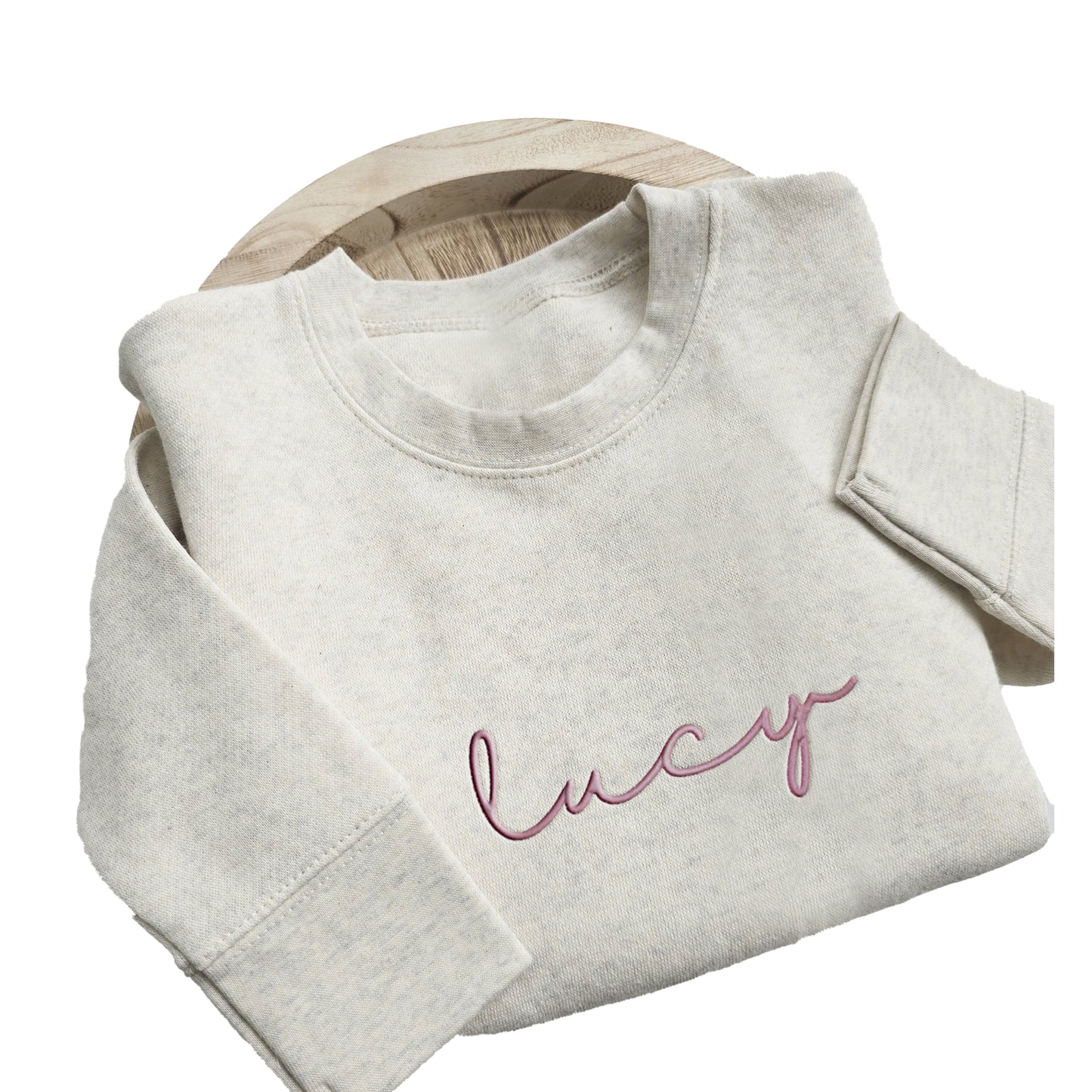 A light colored sweater with "lucy" embroidered on the front in pink thread