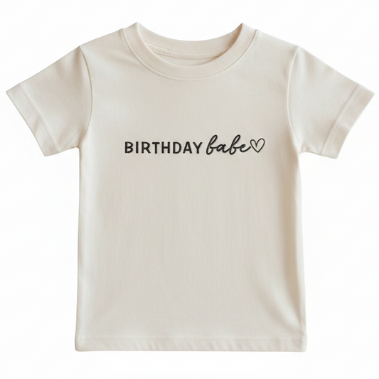 A beige t-shirt with the words "birthday babe" and a heart embroidered on the front in black thread
