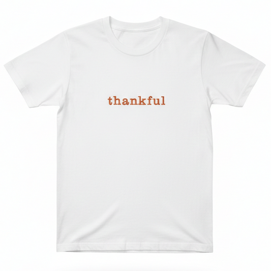 A white T-Shirt with the word "thankful" embroidered on the front in orange thread