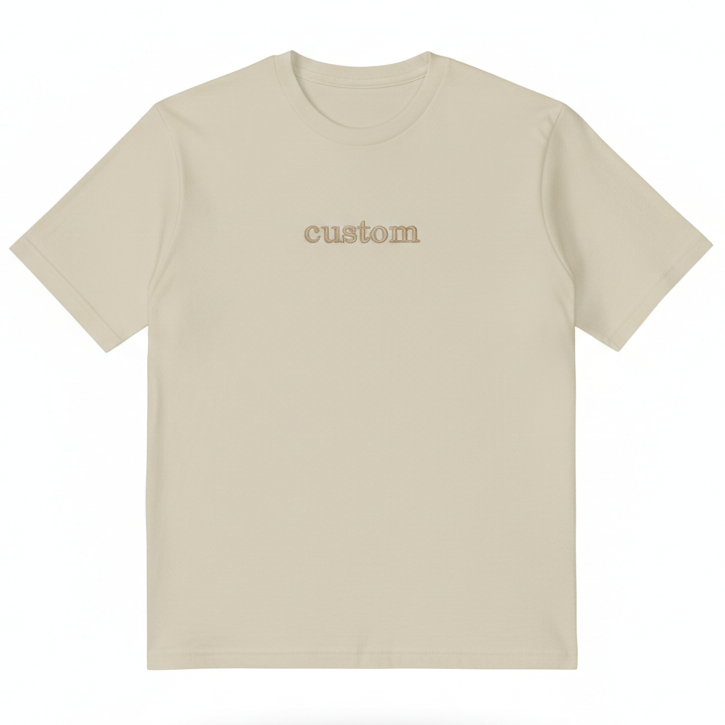 A tan T-Shirt with the word "custom" embroidered on the front in gold thread