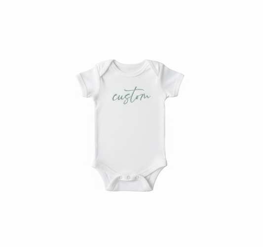 A white colored baby bodysuit with "Custom" embroidered on the front in green thread