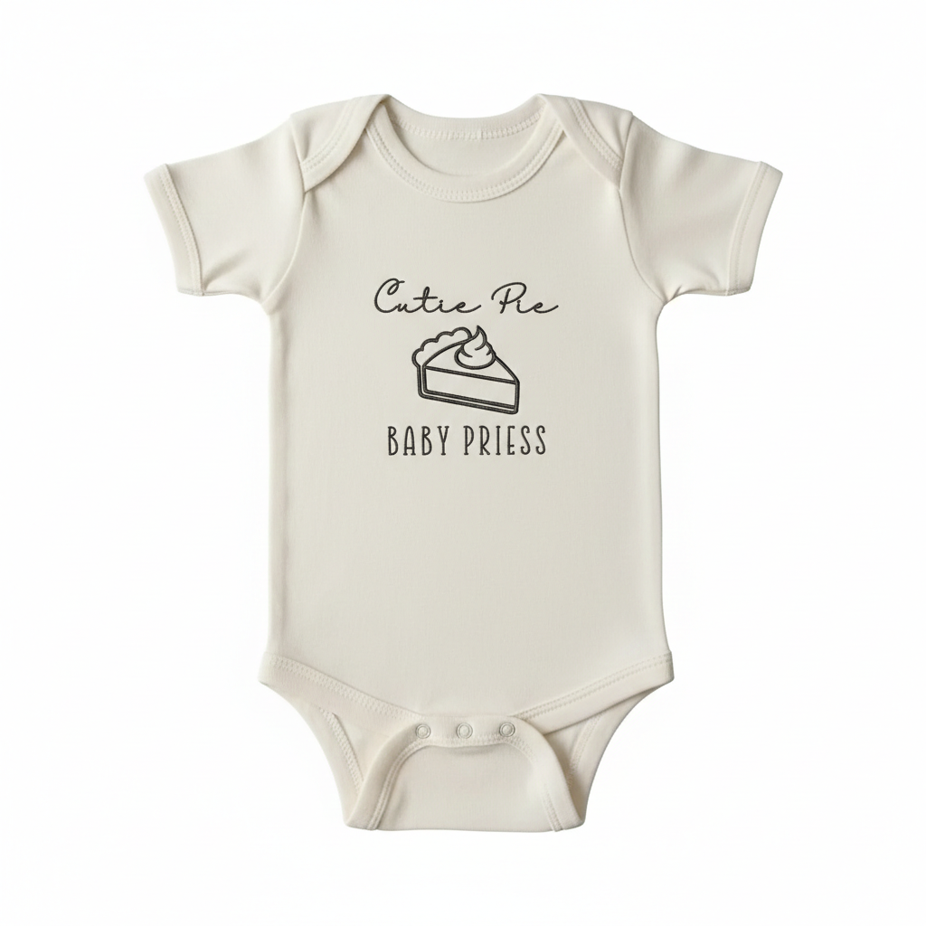 A cream colored baby bodysuit with "Cutie pie Baby Priess" and a slice of pie embroidered on the front in brown thread