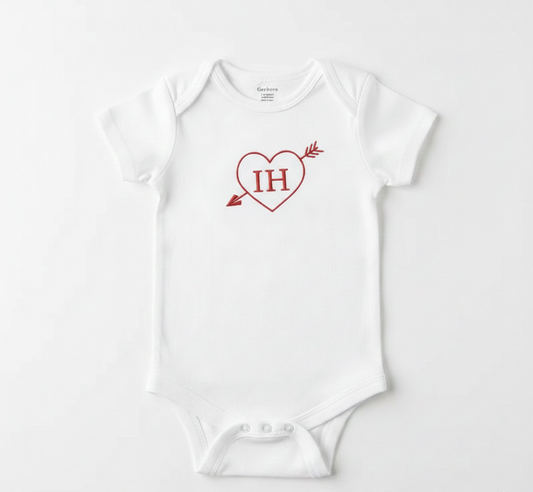 A white colored baby bodysuit with  a cupid's heart and the initials "IH" embroidered on the front in red thread